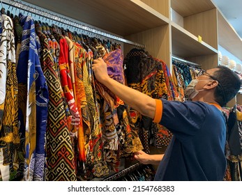 Sidoarjo, Indonesia - May 6, 2022: A man is choosing batik shirts to buy in a batik shop. Batik clothes on display in a boutique.