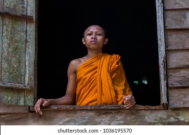 Siem Reap, Siem Reap Province, Cambodia - November 25 2015 : Portrait of a young Buddhist monk standing at a window of a wooden hut against a black background