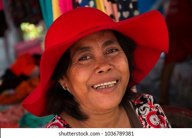Siem Reap, Siem Reap Province, Cambodia - November 27 2015 : Portrait of a woman in a bright red hat at a local market in a village on Highway 6 close to Siem Reap against a colourful background
