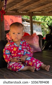 Siem Reap, Siem Reap Province, Cambodia - November 27 2015 : Portrait of a young baby in colourful pyjamas sitting on a wooden floor in the shade in a village on Highway 6 close to Siem Reap