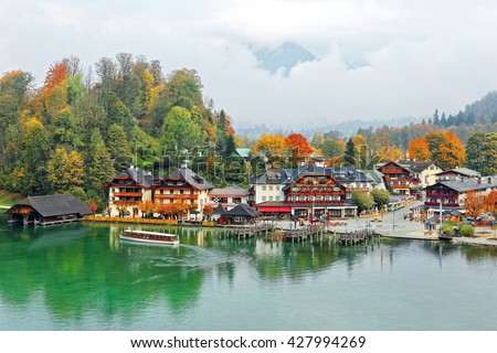 A sightseeing boat cruising on Königssee (King's Lake) surrounded by colorful autumn trees and boathouses on a foggy misty morning. Beautiful scenery of Bavarian countryside in Berchtesgaden, Germany