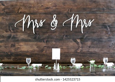 A Sign Behind The Head Table At A Gay Female Wedding Showing The Words Mrs & Mrs.  There Is Copy Space On The White Card For A Photo Or On The Wood Textured Wall.  