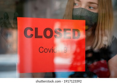 Sign Closed Covid 19 Lockdown On Front Entrance Door As New Normal Shutdown In Restaurant. Woman In Protective Medical Mask Gloves Hangs Closed Sign On Window Of Empty Cafe. Small Business Crisis.