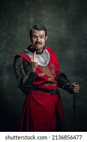 Sign. Comic Portrait Of Funny Medieval Warrior Or Knight With Dirty Wounded Face Gesturing Isolated Over Dark Background. Comparison Of Eras, History, Renaissance Style. Art, Meme