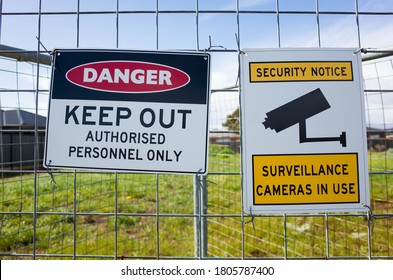 The sign of 'Danger Keep Out Authorised Personnel Only' and ' Security notice Surveillance cameras in use' on a metal construction barrier by a lot of private vacant land. Concept of no trespassing.