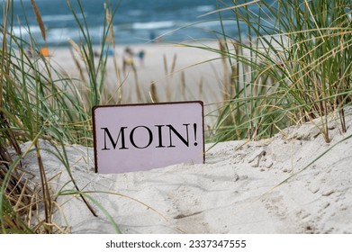 Sign with the German dialect word 'Moin' (Hello) in the sand dunes of an German island in the north sea.