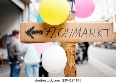 a sign hand-written on cardboard with the inscription flea market on a lamppost with balloons in an urban environment
