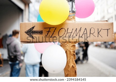 a sign hand-written on cardboard with the inscription flea market on a lamppost with balloons in an urban environment