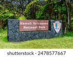 The Sign for Hawaii Volcanoes National Park in front of a vibrant green meadow.