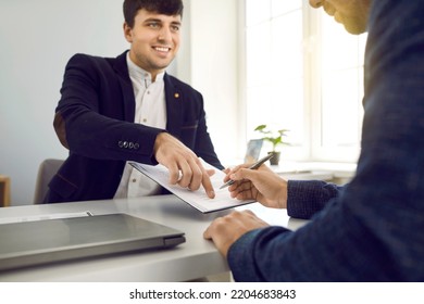 Sign Here Please. Joyful Male Employee Of Bank, Realtor Or Financial Advisor Submits Contract And Indicates Place Of Its Signing. Male Client Signs Contract In Office. Selective Focus.