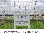 A sign for Imjingak train station along the North Korean and South Korean demilitarized zone. Flags and written notes are attached on the barbed-wire fence.

Translation: all text translated in image.