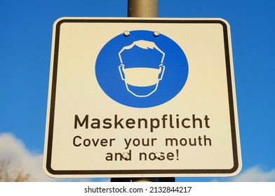 A sign indicates the obligation to wear a mask  Frankfurt, Germany, in Corona times  Blue sky with clouds  Nice blue in blue  - Shutterstock ID 2132844217