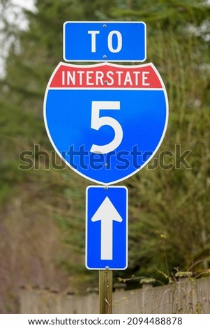 Sign indicates stright ahead to US Interstate 5 in Washington State.  The sign is red white and blue with a vertical arrow for the direction