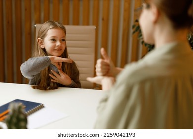 Sign language, smiling deaf-mute little girl communicates with her mother at the table. - Powered by Shutterstock