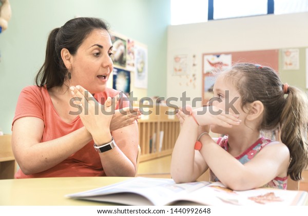 Sign language teacher in a\
extra tutoring class with a deaf child girl using American Sign\
Language.