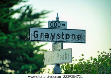 Sign in late day sunset with white and black paint that says Graystone and twin peaks in the historic districts of San Francisco. In California with visible background trees and blue and white sky.