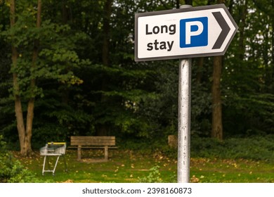 Sign: Long stay parking, with a bench and a shopping trolley in the background, seen in Crowborough, East Sussex, England, UK
