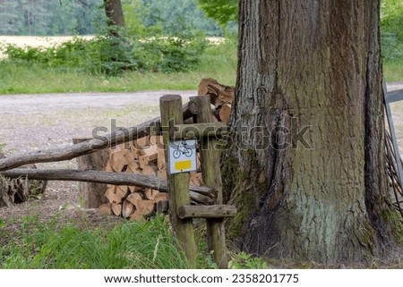 A sign marking a tourist bicycle trail leading through lush forests.A large tree and chopped firewood at a resting point on the tourist bike trail near the village of Czarna Glina (Black Clay).