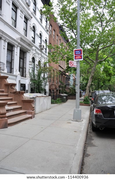 Sign No Honking No Parking on sidewalk of urban\
residential neighborhood in Manhattan New York lined with\
brownstone and limestone\
homes