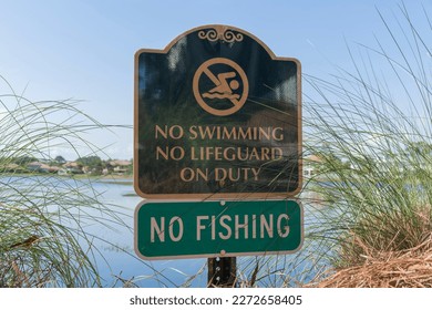 Sign post close-up at Four Prong Lake in Destin, Florida with No Swimming and No Fishing warning. Green signs on a post in the middle of tall grasses against the lake.