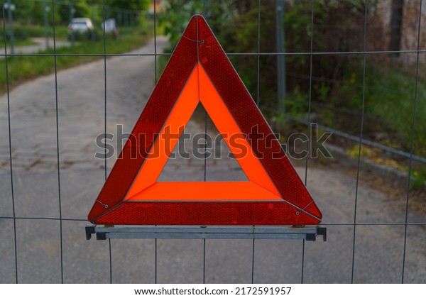 sign red triangle screwed to the fence with a\
mesh behind you can see the road close up sign means an emergency\
stop and attention