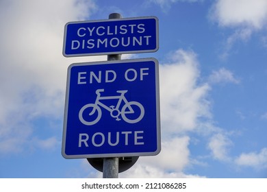 Sign showing End Of Route for cyclists.  Blue road sign under blue cloudy sky. Cyclists Dismount signpost.