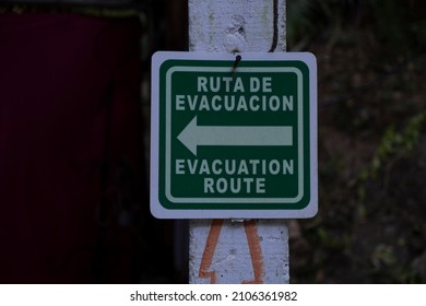 Sign in Spanish and English evacuation route with a direction arrow. Safety, danger, natural disaster concept.