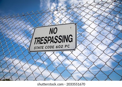 A sign stating No Trespassing on a chain link fence against a blue sky with negative space