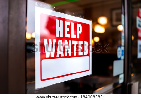Sign text closeup for help wanted with red and white colors by entrance to store shop business building during corona virus covid 19 pandemic