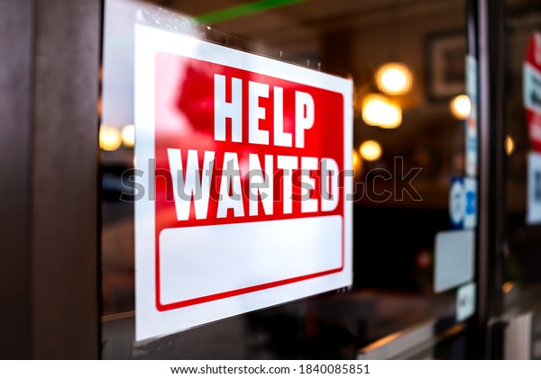 Sign text closeup for help wanted with red and\
white colors by entrance to store shop business building during\
corona virus covid 19\
pandemic