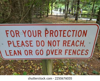 A sign warning people not to reach, lean, or go over fences. - Shutterstock ID 2250676035