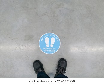 Signage to advise on keeping distance seen on the floor of a warehouse with safety boots ahead of it.