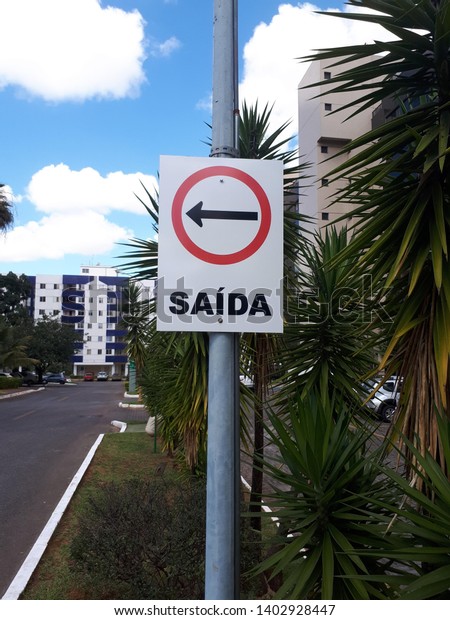 Signage plate, galvanized steel, electrostatic\
painting, reflective adhesive, indicating with arrow, the following\
direction, urban landscape in the Brazilian capital with blue sky\
and white clouds.