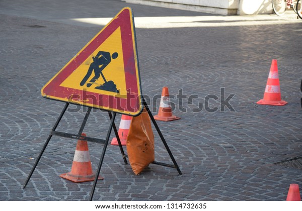 signals cones\
and a safety sign of danger, men at work in the middle of a old\
road in the center of an Italian\
town