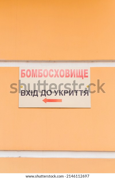 Signboard with inscription in Ukrainian - Bomb\
Shelter. Refuge entrance - on orange wall. War in Ukraine 2022.\
Russian invasion. Vertical\
shot