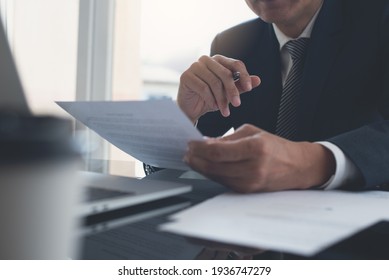 Signing Contract, Business Agreement And Deal Concept. Closeup Businessman Reading Business Contract Documents At Desk With Laptop Computer, Busy With Paperwork. Man Manager Proofing Report At Office