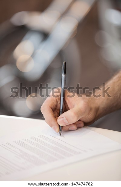 Signing the paper. Close-up of\
hand signing the paper with a motorcycle wheel on the\
background