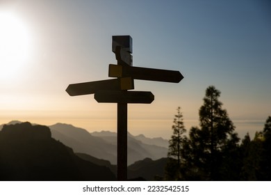 signpost in the mountain at sunset. Silhouette of a sign with four directions with mountains and sunset in the background