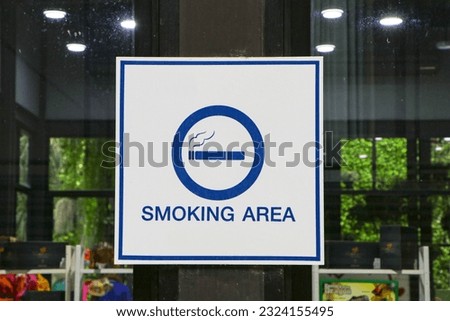 Signs or sign symbolize white plastic with blue letters smoking area background is glass and lamps are blurred. It is symbol notifying people to use service in restaurants or parks.