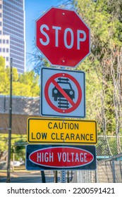 Signs: Stop, Do not drive on tracks, Caution low clearance, and High Voltage- downtown Tucson, AZ. Multiple road signs on a post against the view of a street and buildings at the back. - Shutterstock ID 2200591421