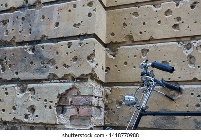 Signs Of War By Bullet Holes From WW2 On Berlin Building Wall With An Old Parked Bicycle Leaned Against It.