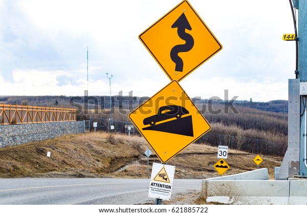 Signs warning of a windy road with a steep\
incline and surveillance camera, image of old antique like car as\
the car going down the incline\
