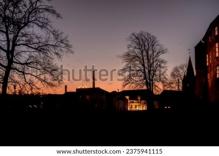 sihouette of building and bare tree in the sunset at winter time with orange sun colour 