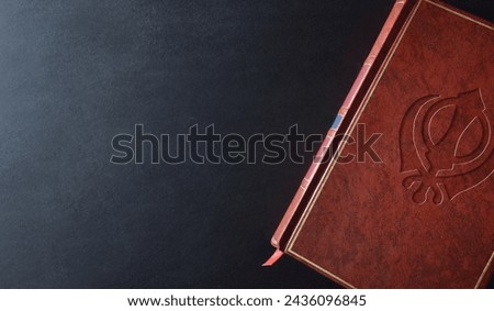 Sikh culture and religion book with religious symbol engraved on the brown leather cover on a black table. Top view.