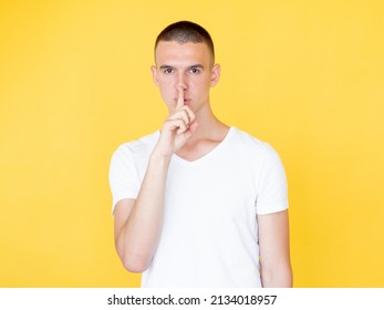 Silence Gesture. Conspirator Man. Censor Expression. Serious Hipster Guy In Casual White T-shirt Holding Shush Finger On Mouth Isolated Yellow.