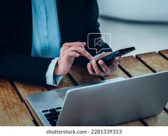 Silent mode concept. Silent or mute sound icon turn activated on appear in speech bubble on mobile smart phone in hand while business person work with laptop computer on desk in office or workplace.