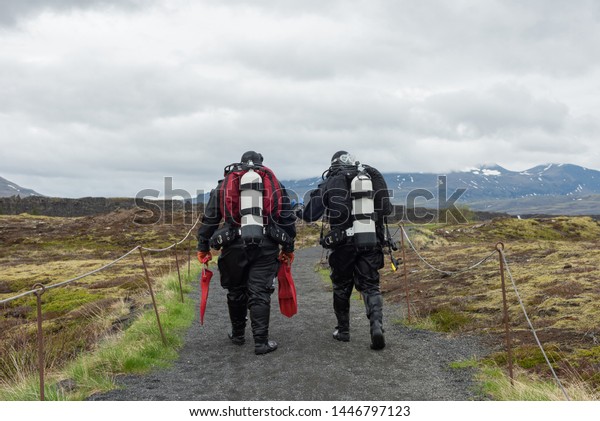 SILFRA, ICELAND - MAY 20, 2019: Scuba divers walking\
on a path after a diving at Silfra rift, the place where Eurasian\
and the American tectonic plate are divided in Thingvellir National\
Park