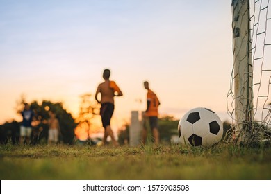 Silhouette Action Sport Outdoors Of Diversity Of Kids Having Fun Playing Soccer Football For Exercise In Community Rural Area Under The Twilight Sunset Sky.