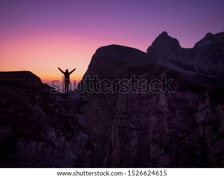 SILHOUETTE: Active young woman outstretches her arms in victory as she observes the golden sunset from a scenic mountaintop. Excited tourist girl reaches the summit on a breathtaking autumn evening.