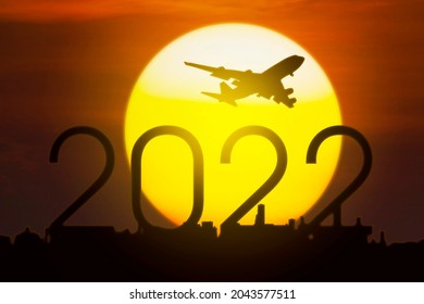Silhouette of aircraft flying in the sky above 2022 numbers and city with sunrise sky background
